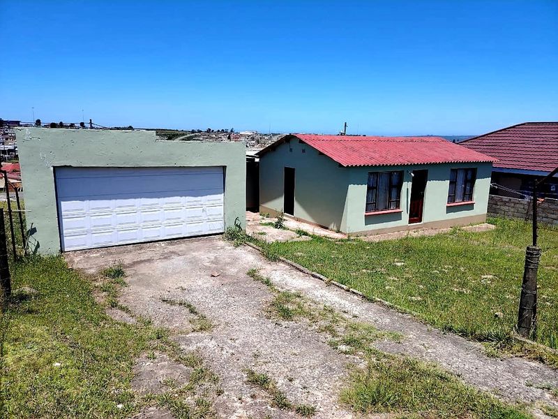 Front view of a detached house featuring a separate garage, concrete driveway, and a corrugated metal roof, set on a grassed plot.