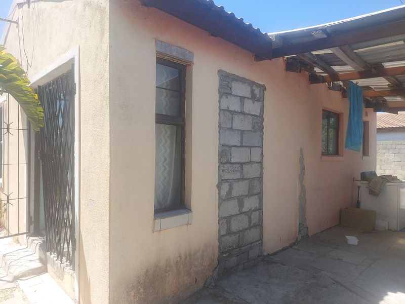 Rear exterior view of the property showing a covered patio area, a blocked-up doorway, and visible signs of exterior wall deterioration.