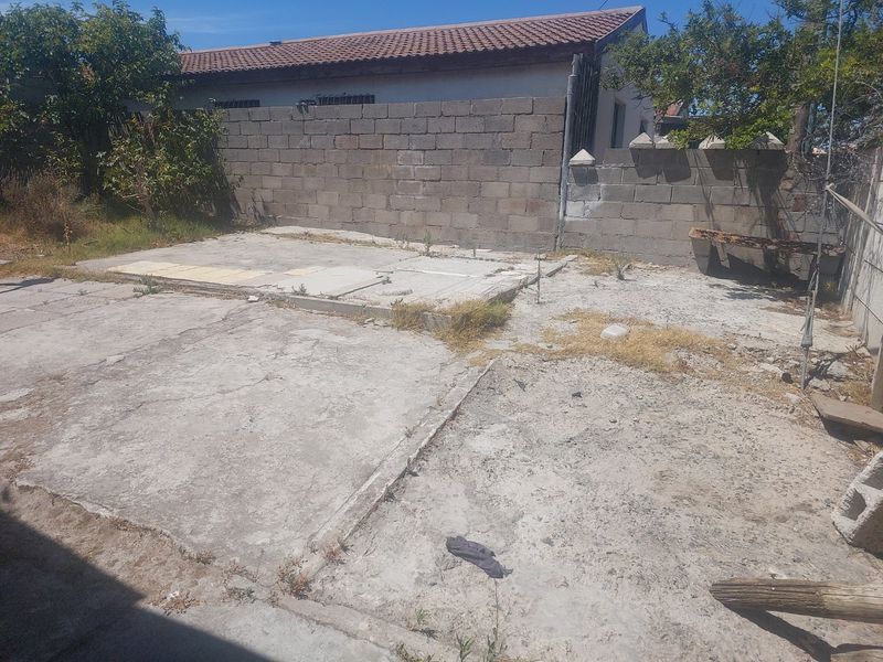 A rear outdoor area featuring a concrete slab and cinder block boundary walls, requiring landscaping and surface repairs to improve usability.
