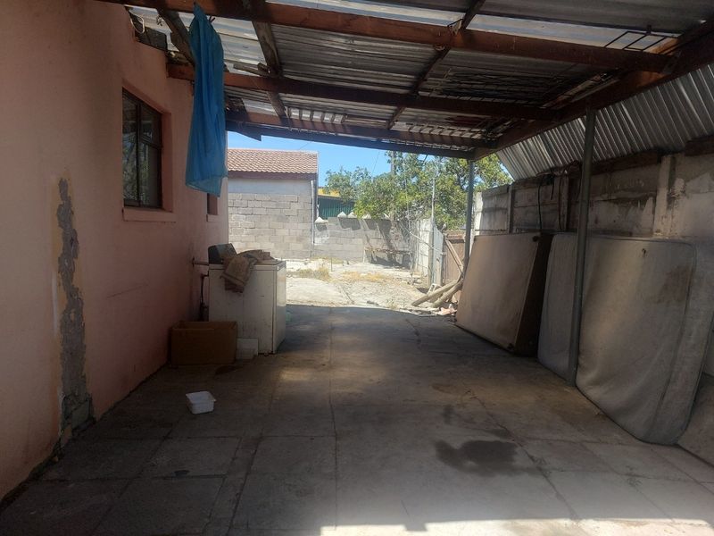 A covered outdoor patio area featuring concrete paving and a corrugated metal roof structure, requiring maintenance and repair to the roof and wall finishes.