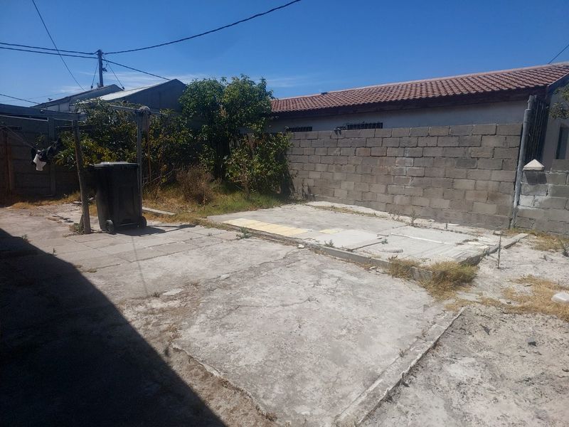 A rear exterior area featuring concrete paving and a cinder block boundary wall, requiring landscaping and surface repairs to improve the outdoor space.
