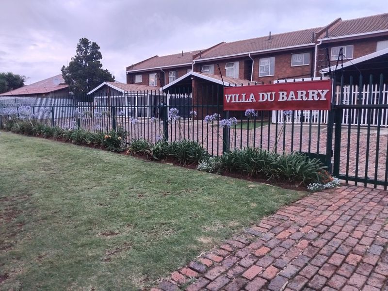 Front view of the Villa Du Barry apartment complex featuring brick facade, paved driveway, and secure metal perimeter fencing.