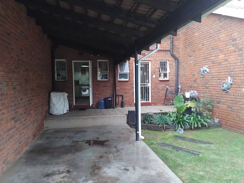 A rear exterior view of the apartment featuring a covered patio area, brick facade, and access to the kitchen and rear entrance.