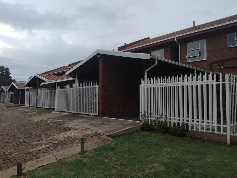 Exterior view of an apartment complex featuring brick facades, covered carports, and secure perimeter fencing with paved driveway access.