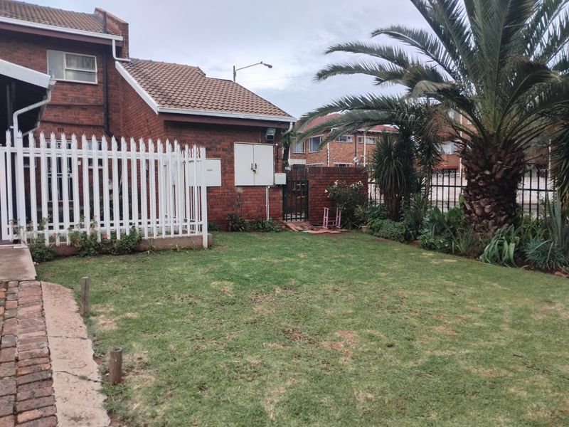 A private rear garden area featuring a brick facade, established palm tree, paved walkway, and secure perimeter fencing.