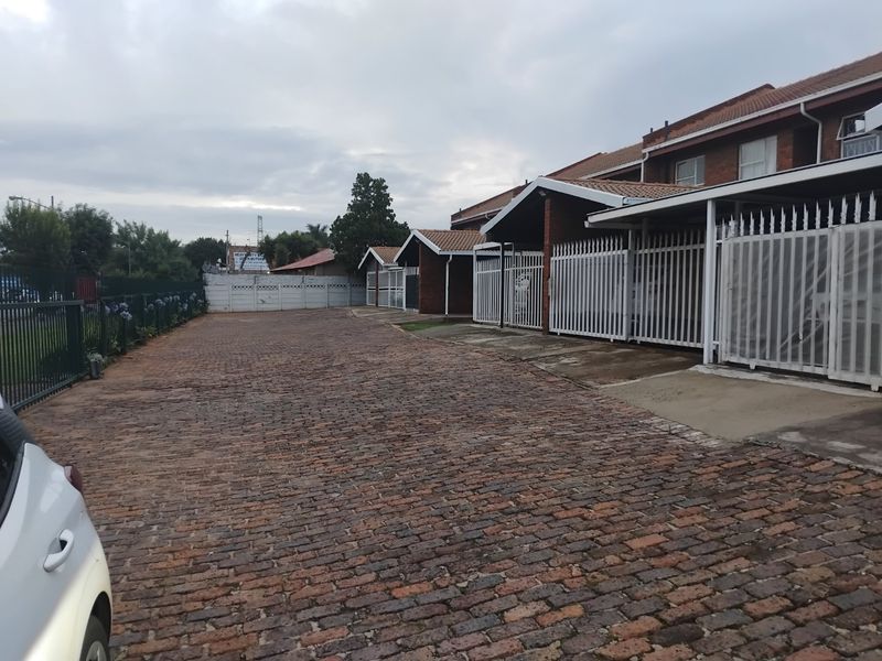 Exterior view of an apartment complex featuring a brick-paved driveway, secure metal fencing, and covered carport parking bays.
