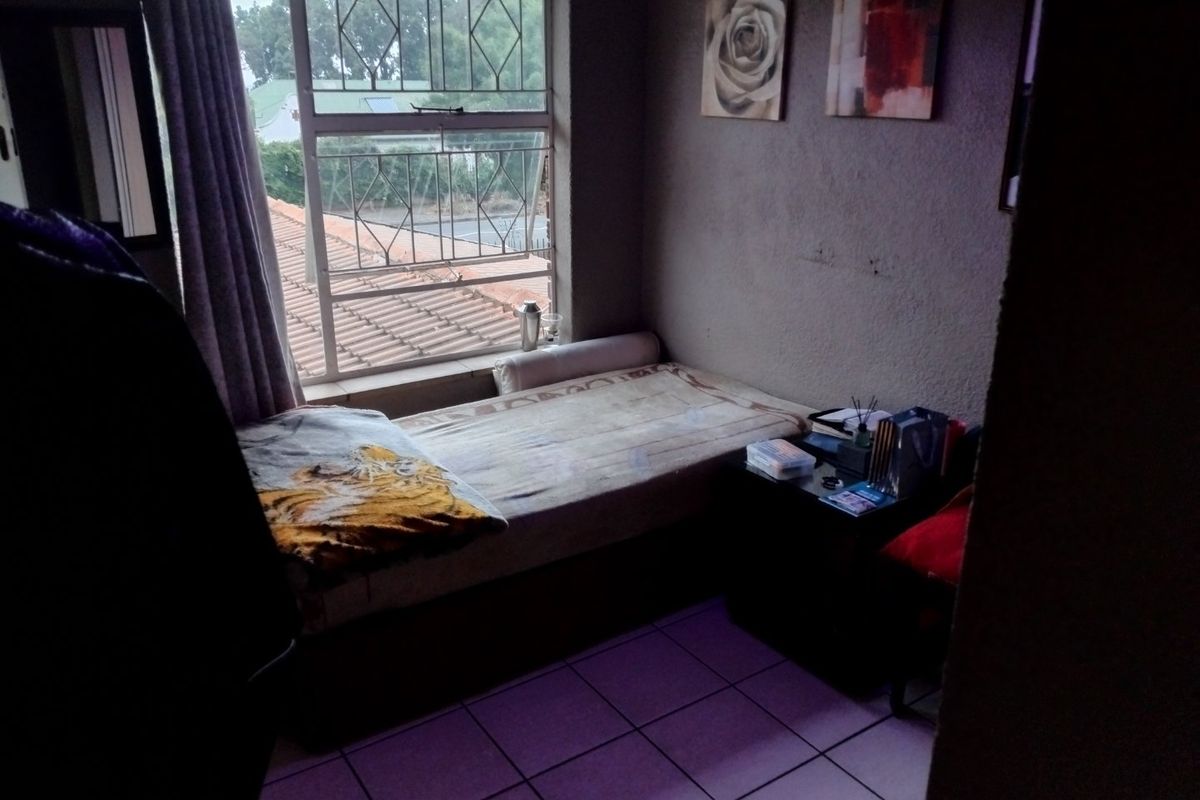 A compact bedroom featuring tiled flooring and a window with security bars, offering a functional space that could benefit from cosmetic updates.