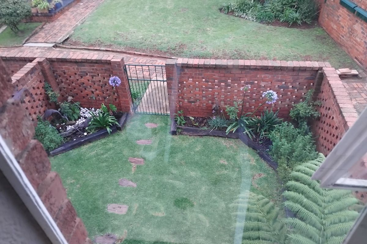 An elevated view of a private rear garden featuring a brick boundary wall, metal gate, manicured lawn, and established garden beds with stone pathways.