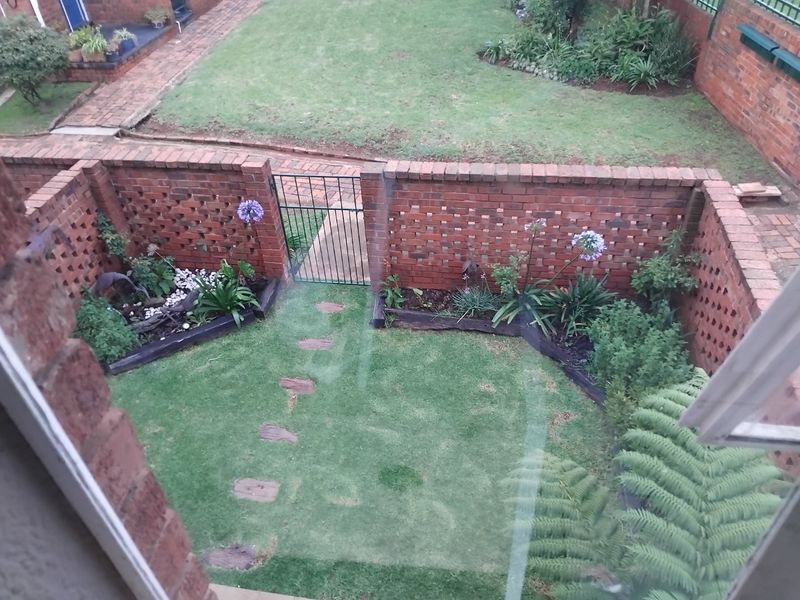 An elevated view of a private rear garden featuring a brick boundary wall, metal gate, manicured lawn, and established garden beds with stone pathways.