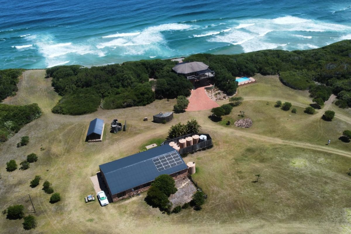 Aerial view of a coastal farm property featuring multiple buildings, solar panels, water storage tanks, and a swimming pool overlooking the ocean.