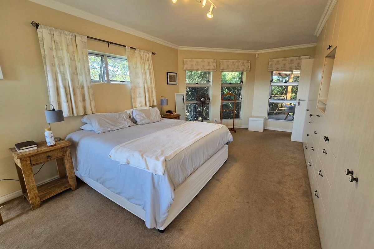 Spacious bedroom featuring built-in cupboards, neutral carpeting, and multiple windows providing natural light and garden views.
