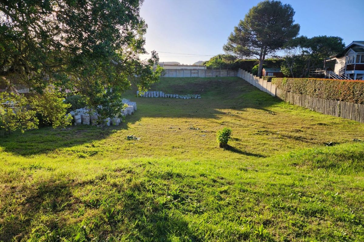 A spacious, grassed residential plot featuring established trees, perimeter fencing, and a retaining wall, offering a clear area for potential development.