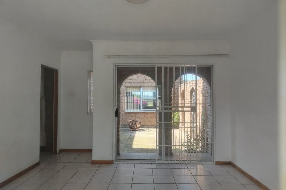 An empty living room featuring ceramic floor tiles and a sliding glass door with a security gate, providing access to an outdoor patio area.