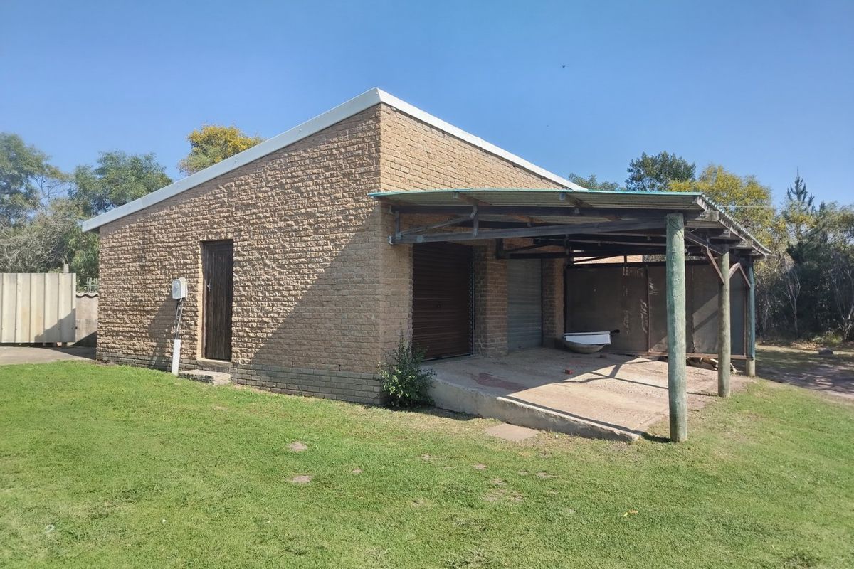 A detached brick garage featuring a covered carport area, metal roller doors, and a concrete driveway on a rural property.