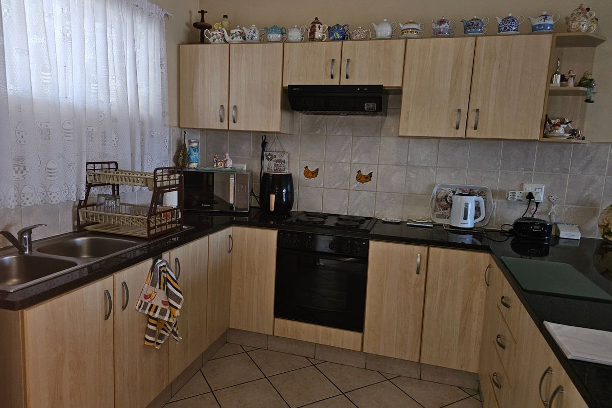 Functional kitchen featuring light wood-finish cabinetry, dark granite countertops, built-in oven, electric hob, and tiled flooring.