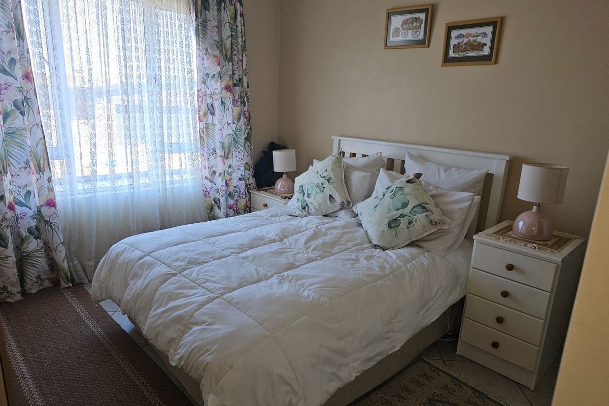 A cozy bedroom featuring tiled flooring and a large window, providing a comfortable and functional sleeping space.
