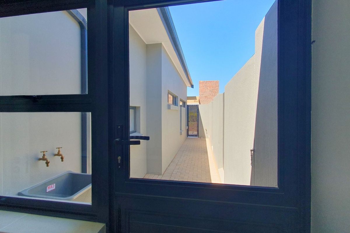 A view through a doorway looking out onto a paved side walkway with a boundary wall and utility sink area.