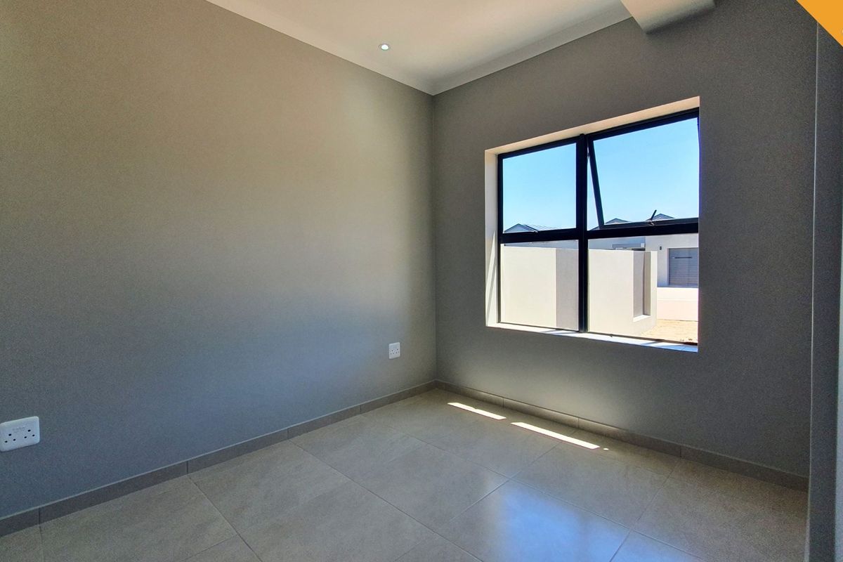 A bright, modern, and empty bedroom featuring neutral grey walls, large aluminium-framed windows, and clean tiled flooring.