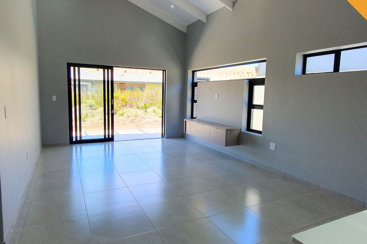Spacious, modern living area featuring high vaulted ceilings, large sliding glass doors, and a sleek built-in media console with neutral tiled flooring.