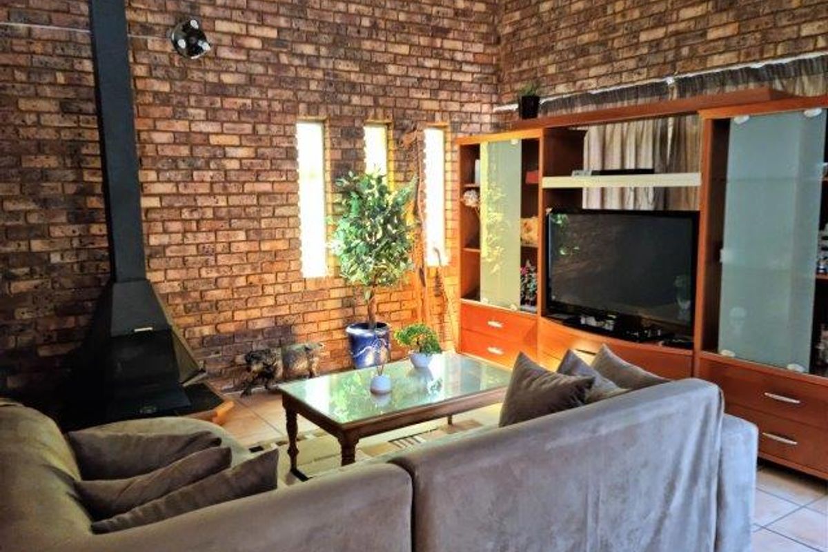 Cozy living room featuring a prominent exposed brick wall, a black freestanding fireplace, and tiled flooring, creating a warm and rustic atmosphere.