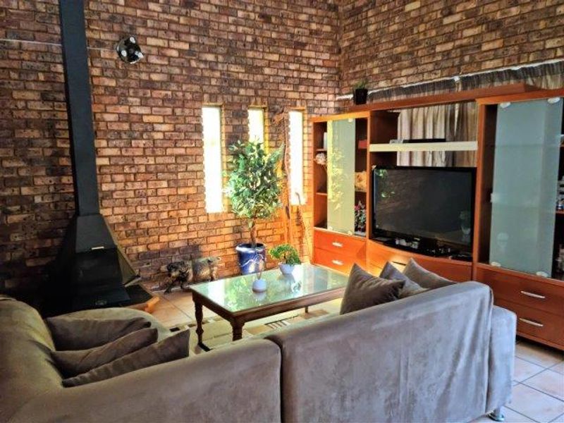 Cozy living room featuring a prominent exposed brick wall, a black freestanding fireplace, and tiled flooring, creating a warm and rustic atmosphere.