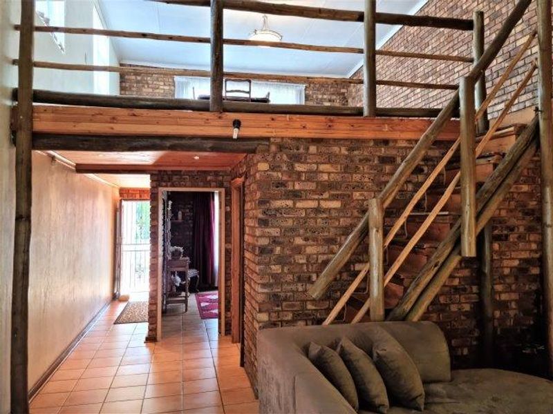 Living area featuring exposed brick walls, a timber staircase leading to a mezzanine level, and tiled flooring throughout.