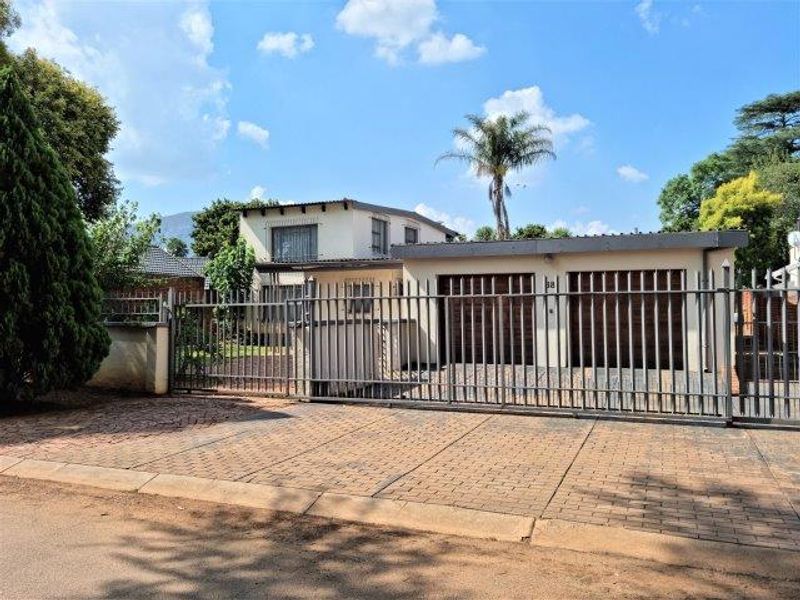Front exterior view of the property featuring a double garage, paved driveway, and secure metal perimeter fencing.