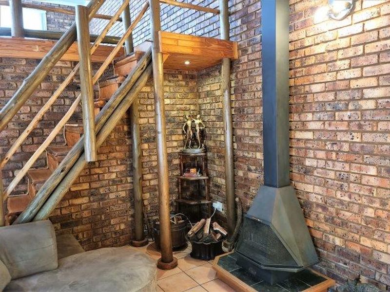 Living area featuring exposed brick walls, a rustic timber staircase, and a modern freestanding fireplace set on a tiled hearth.