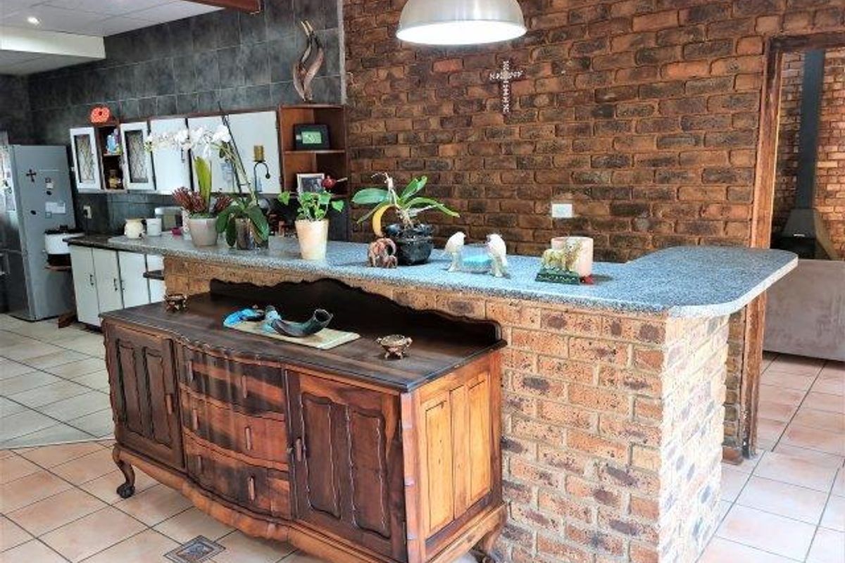 Kitchen area featuring a rustic exposed brick wall, granite-topped breakfast bar, and tiled flooring, offering a warm and characterful space.