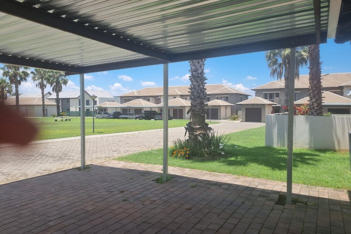 A view from a covered carport looking out over a paved driveway and communal garden area within the apartment complex.