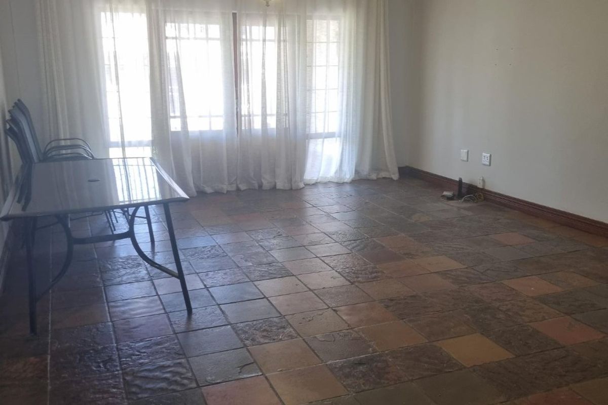 A spacious living area featuring rustic tiled flooring, an installed air conditioning unit, and natural light streaming through large glass doors.