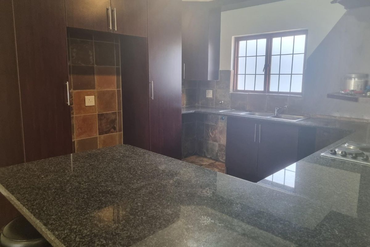 A functional kitchen featuring dark cabinetry, granite countertops, a double basin sink, and a built-in hob with tiled backsplash.