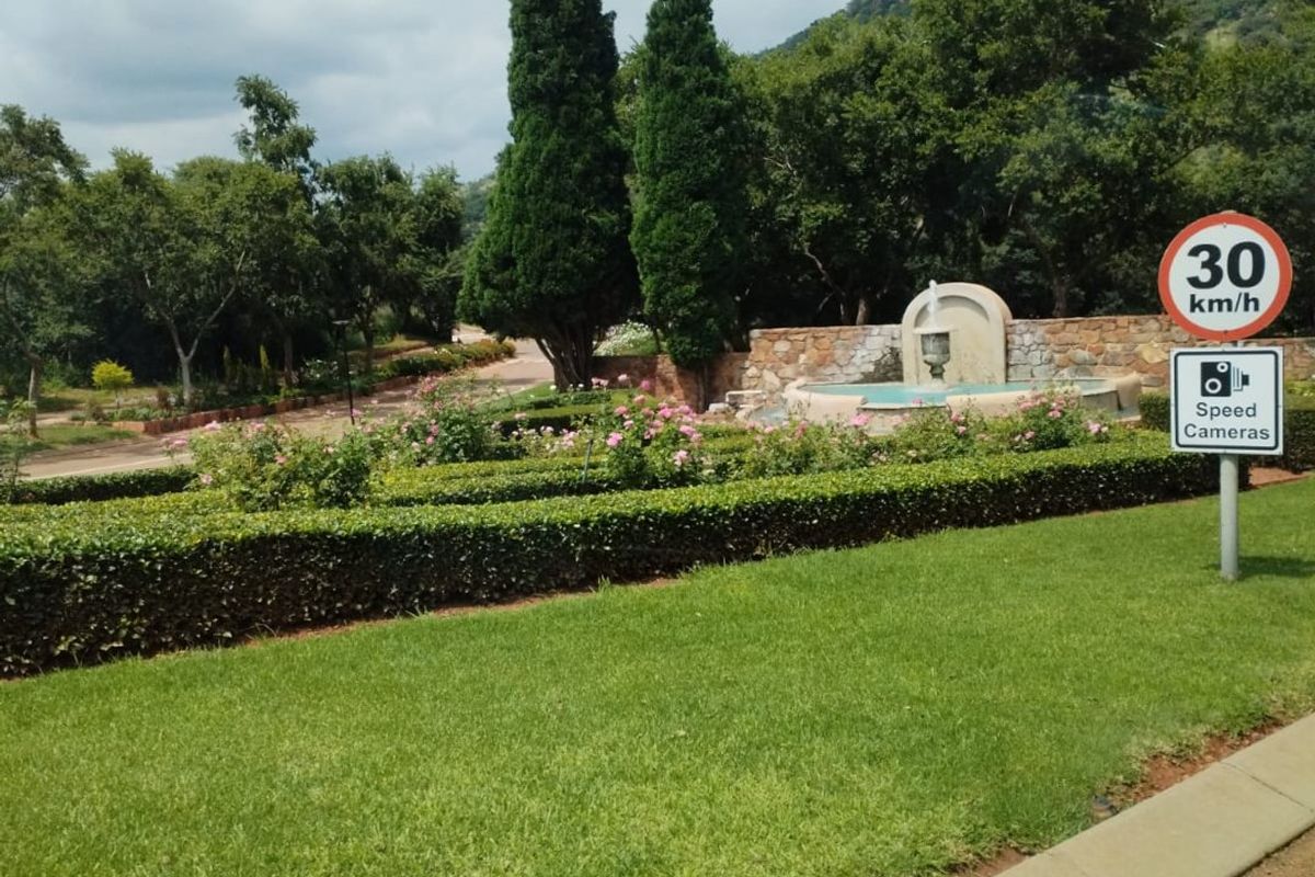 A well-maintained garden area featuring a stone fountain, manicured hedges, and mature trees within a residential estate setting.