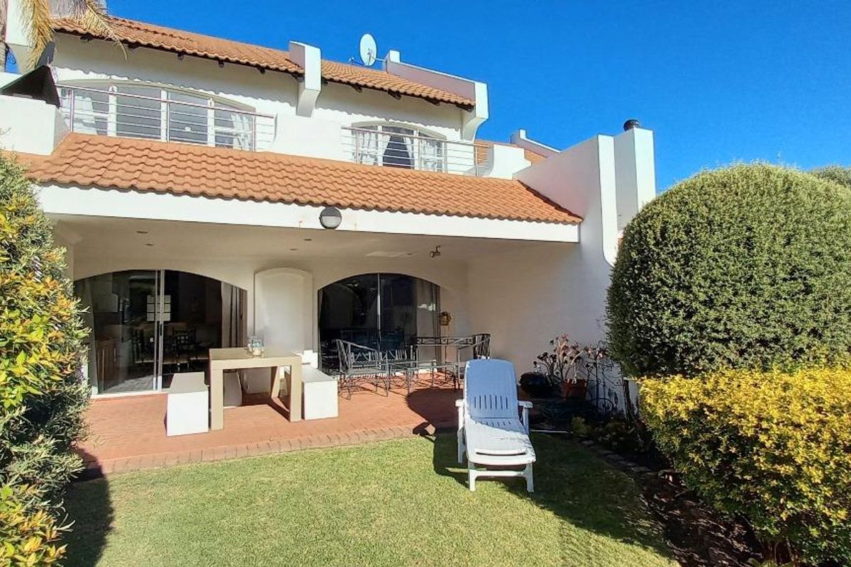 Rear view of the townhouse featuring a covered patio, a private garden, and an upper-level balcony with metal railings.