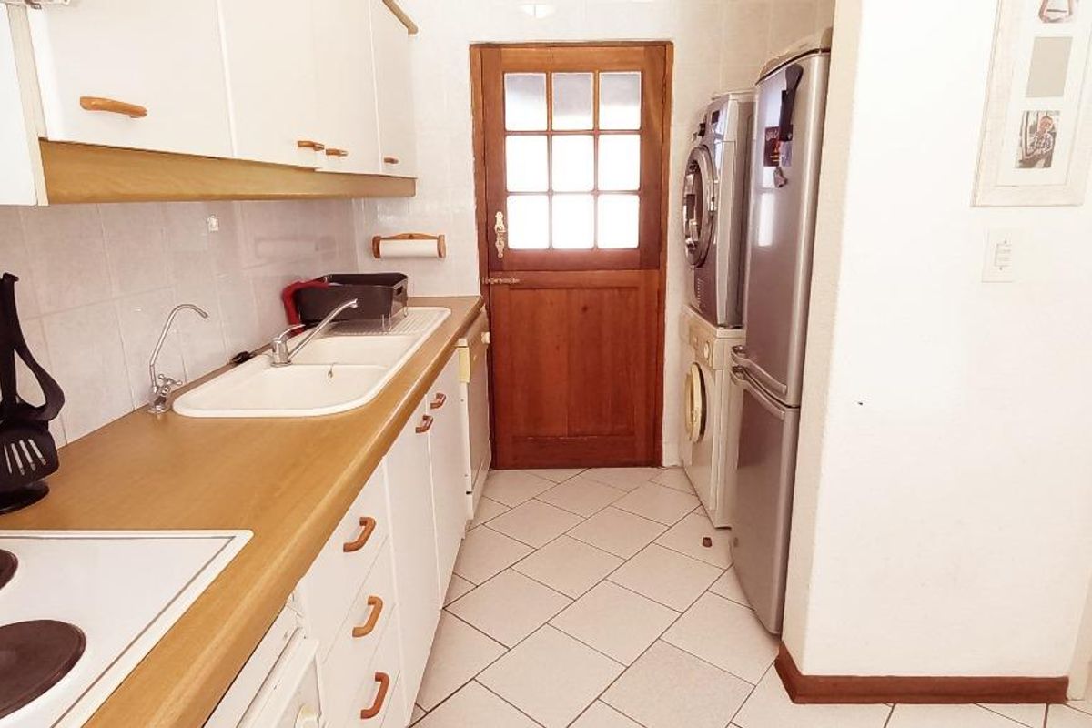 A functional kitchen featuring white cabinetry, laminate countertops, a double sink, and an electric hob, with direct access to an exterior door.