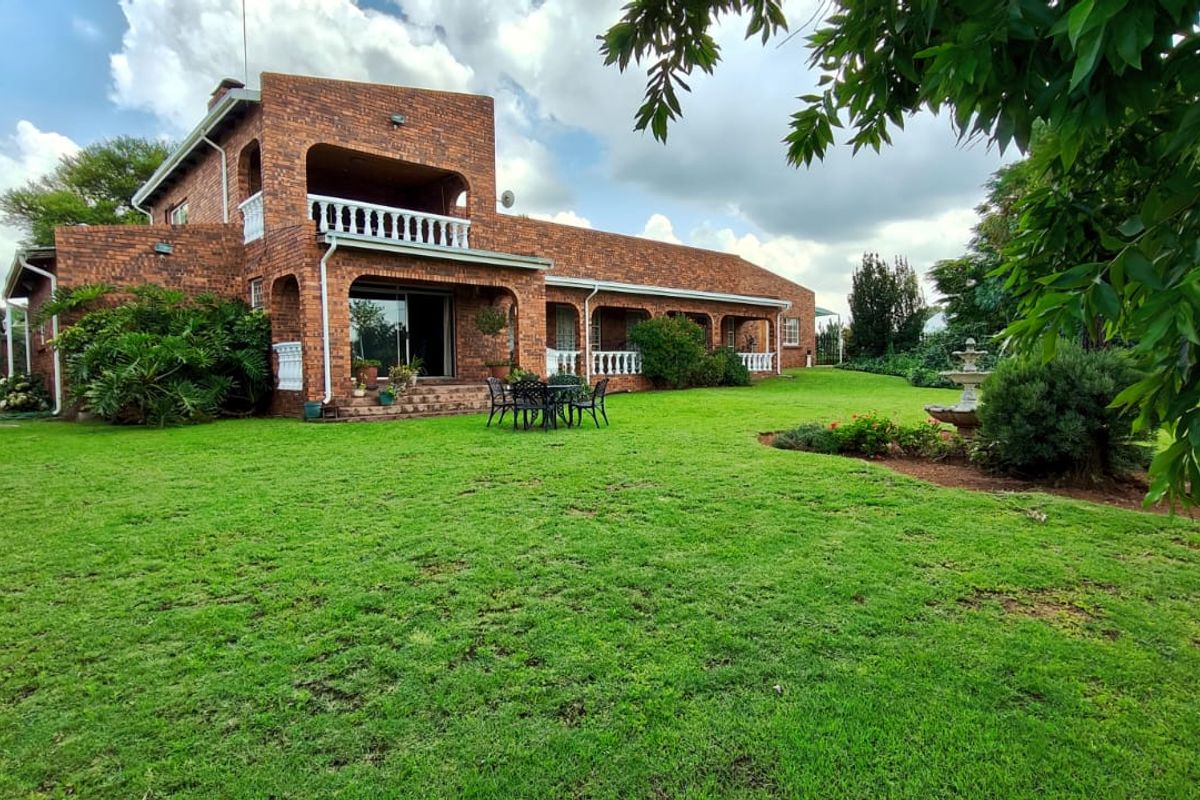 A spacious rear garden view featuring a two-story face brick house with a covered patio, balcony, and established lawn.