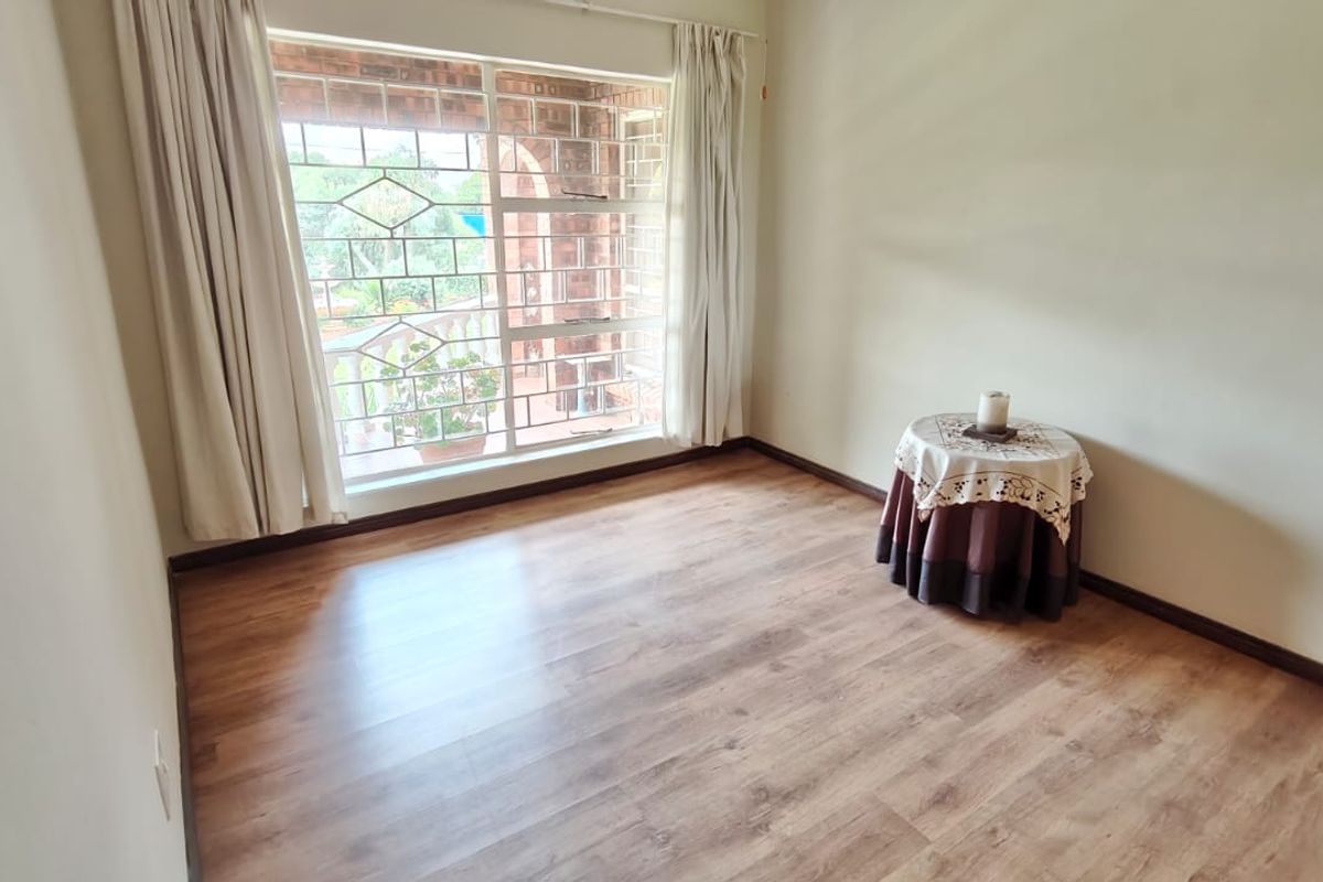 A bright, empty bedroom featuring laminate flooring and a large window with security bars, offering a clean and neutral space ready for personalization.