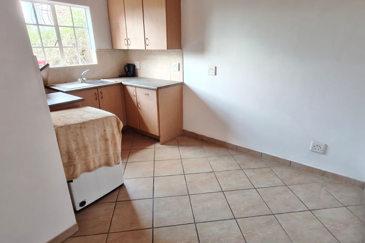 A functional kitchen featuring laminate cabinetry, tiled flooring, and a stainless steel sink, offering a clean and simple layout ready for updates.