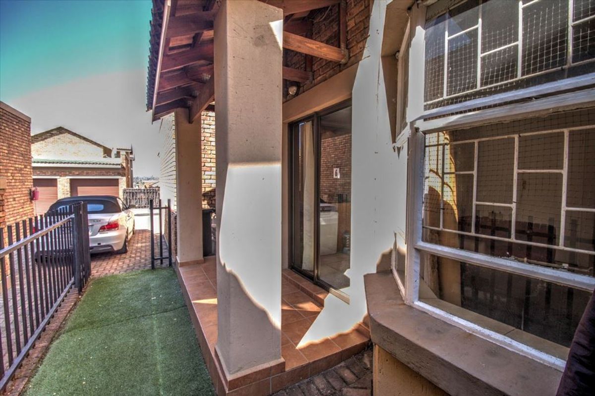 A covered patio area featuring tiled flooring, exposed timber rafters, and a sliding glass door entrance with security bars.