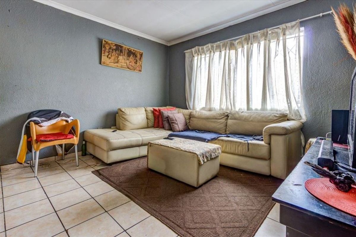 A living room featuring tiled flooring and cornicing, currently requiring cosmetic updates to the wall finishes and flooring.