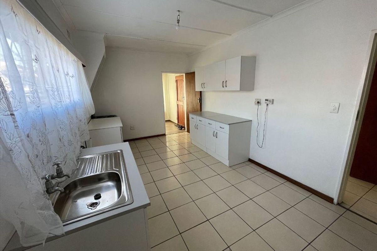 A functional, empty kitchen space featuring white built-in cabinetry, a stainless steel sink, and neutral ceramic floor tiles.