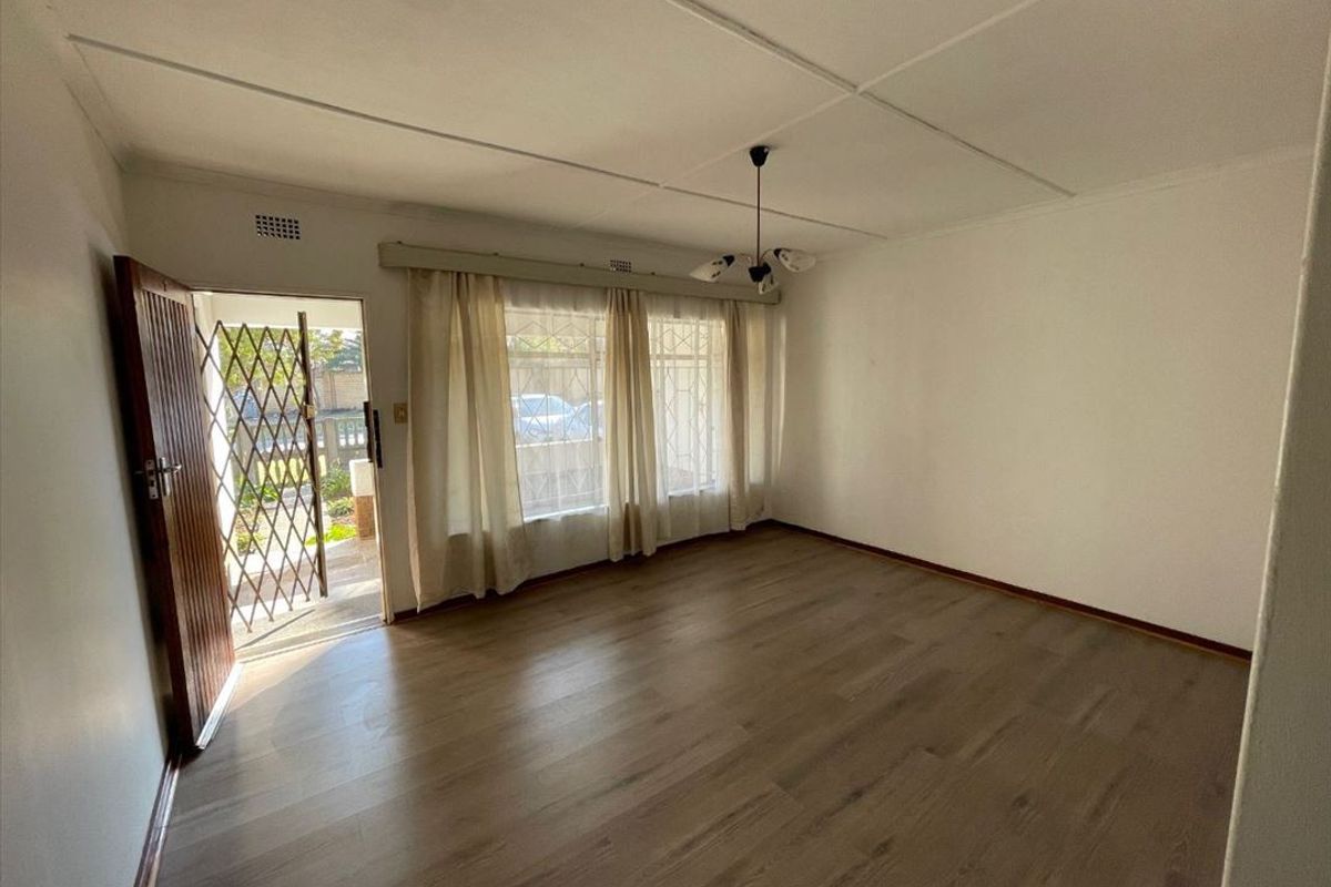A bright, empty living room featuring laminate flooring, a security gate at the entrance, and neutral walls, offering a blank canvas for personalization.