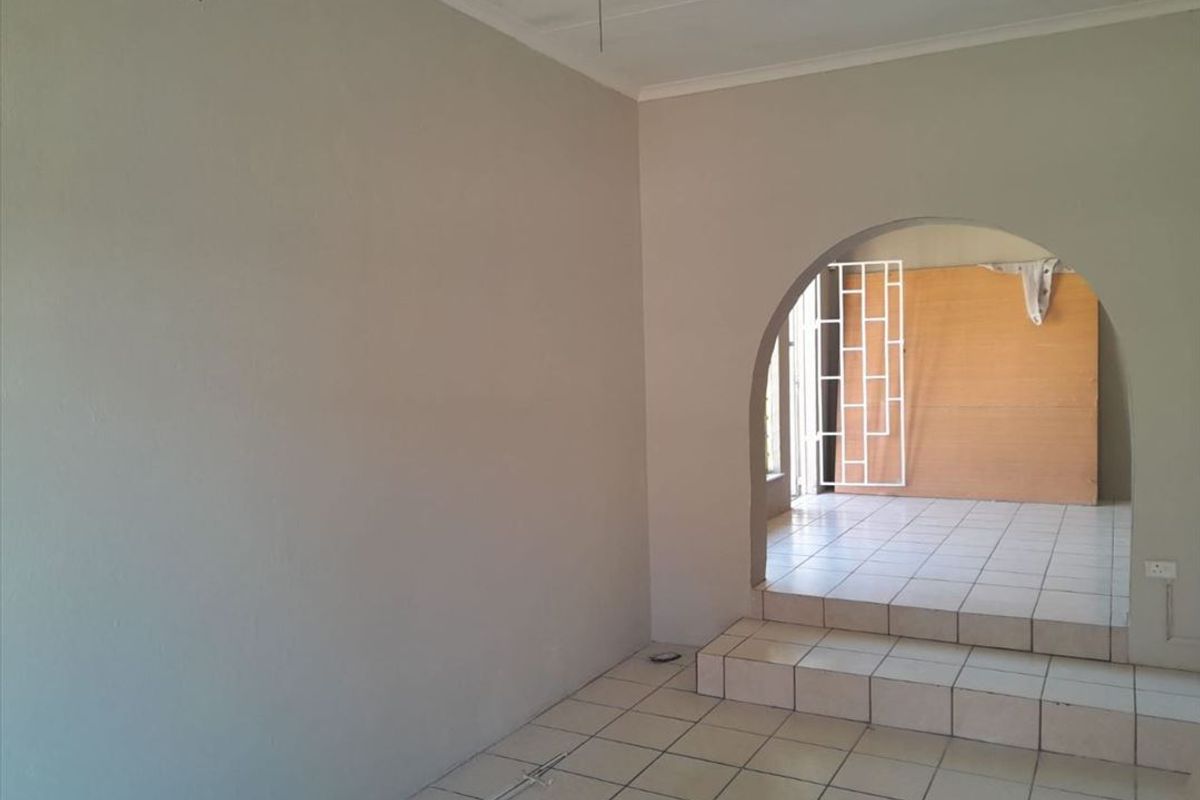 An empty living area featuring tiled flooring, a distinctive arched doorway leading to an adjacent space, and a security gate.