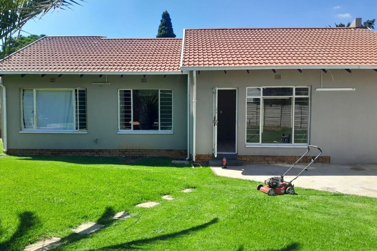 Rear view of a single-story house featuring a tiled roof, steel-framed windows with security bars, and a concrete patio area overlooking the lawn.