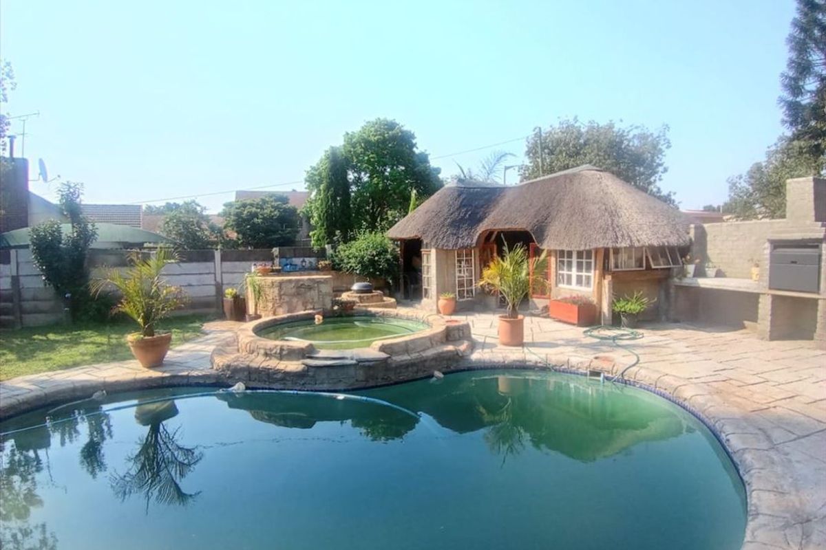 Outdoor entertainment area featuring a swimming pool, raised spa, and a thatched lapa with a built-in braai facility.