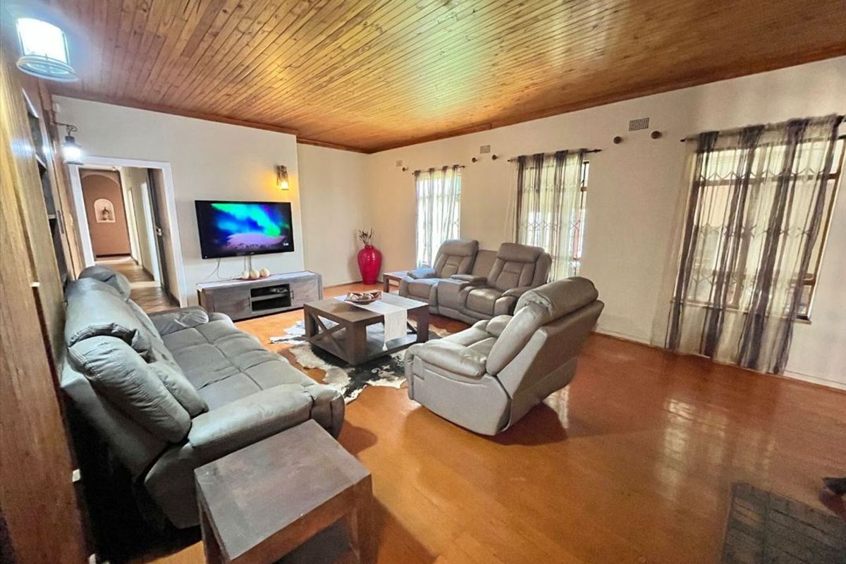 Spacious living room featuring warm timber ceilings, polished hardwood flooring, and wall-mounted lighting fixtures.