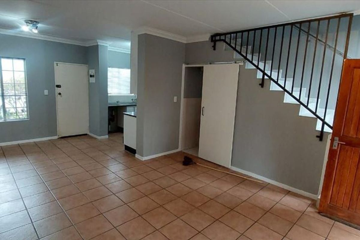 Open-plan living area featuring tiled flooring, a staircase with metal railing, and access to a compact kitchen space.