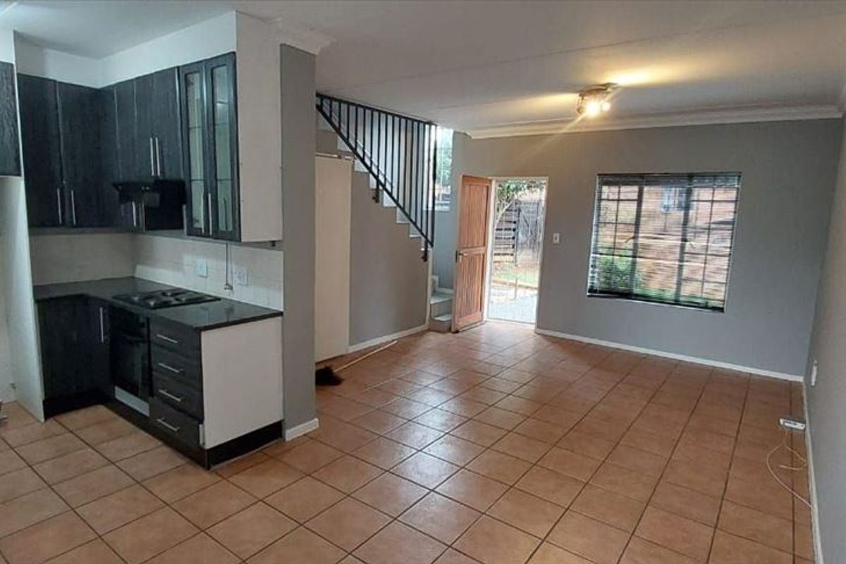 Open-plan living area featuring a kitchen with built-in cabinetry, hob, and oven, tiled flooring, and direct access to the exterior via a security gate.