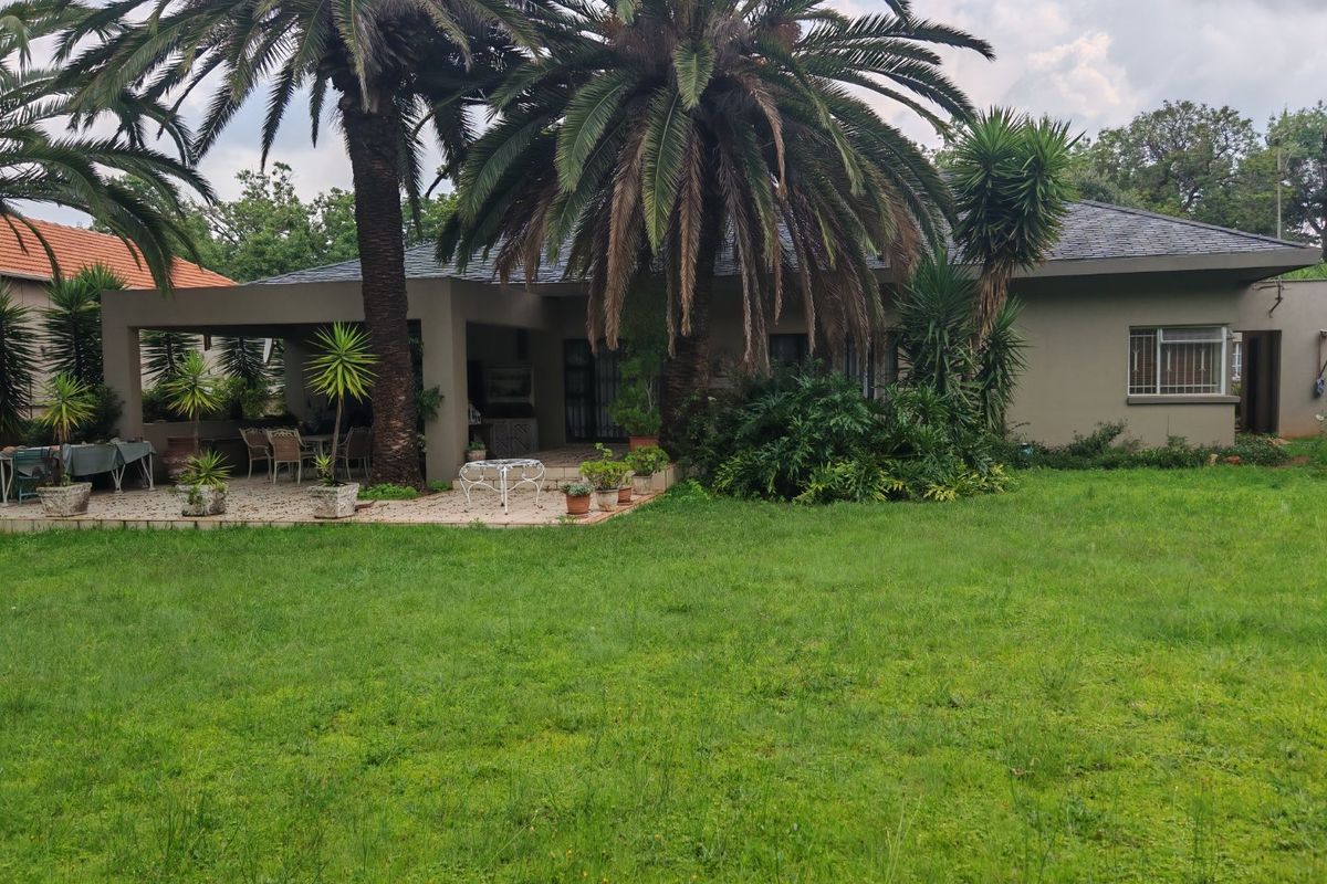 Rear view of the house featuring a covered patio area, built-in braai, and a spacious garden with mature palm trees.