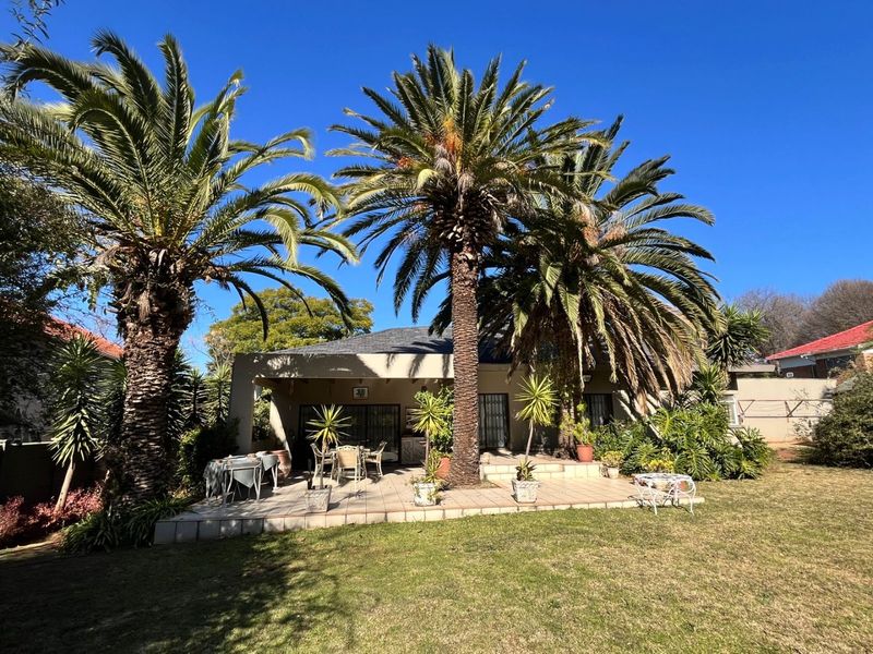 A spacious rear patio area featuring tiled flooring and sliding glass doors, set within a well-maintained garden with mature palm trees.